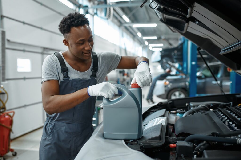 Male worker changes oil in engine, car service